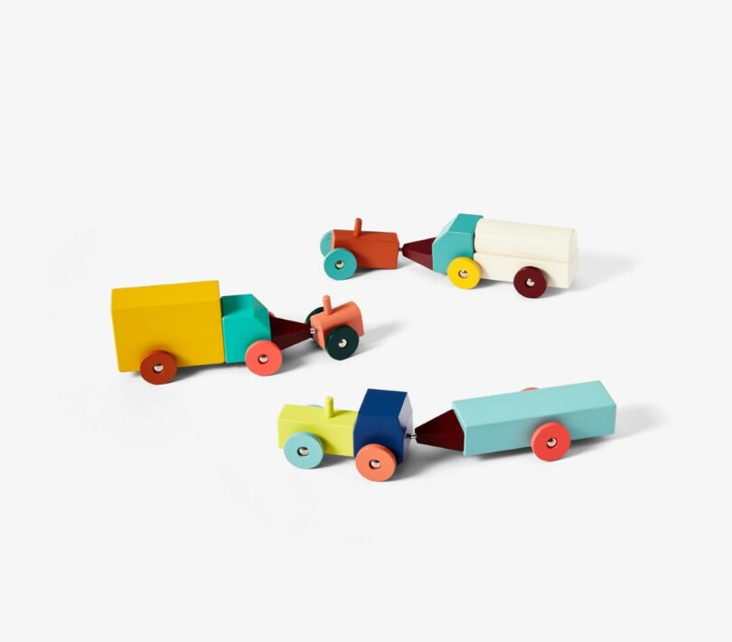 Four colorful wooden toy trucks are arranged on a plain white background