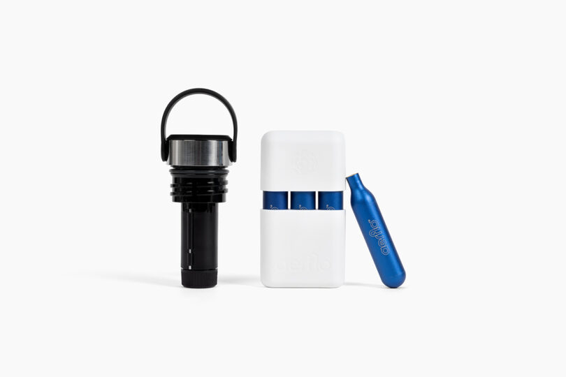 A black and silver bottle opener stands next to a white case holding two blue CO2 cartridges, with an additional cartridge placed beside it.