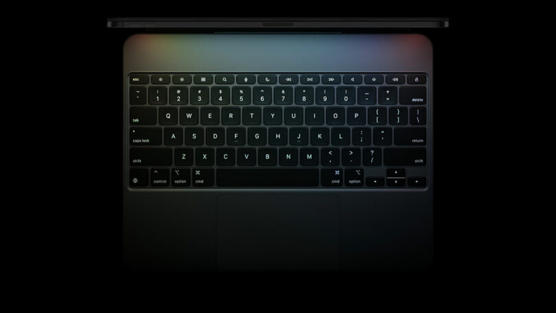 Top view of a laptop keyboard and trackpad on a dark background, with faint colored reflections on the upper edge of the device—reminiscent of the sleek design found in the iPad Pro.