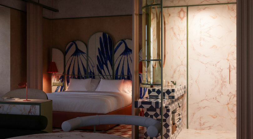 A modern hotel room with a double bed, blue-patterned headboard, geometric-tiled sink area, and marble-patterned shower.