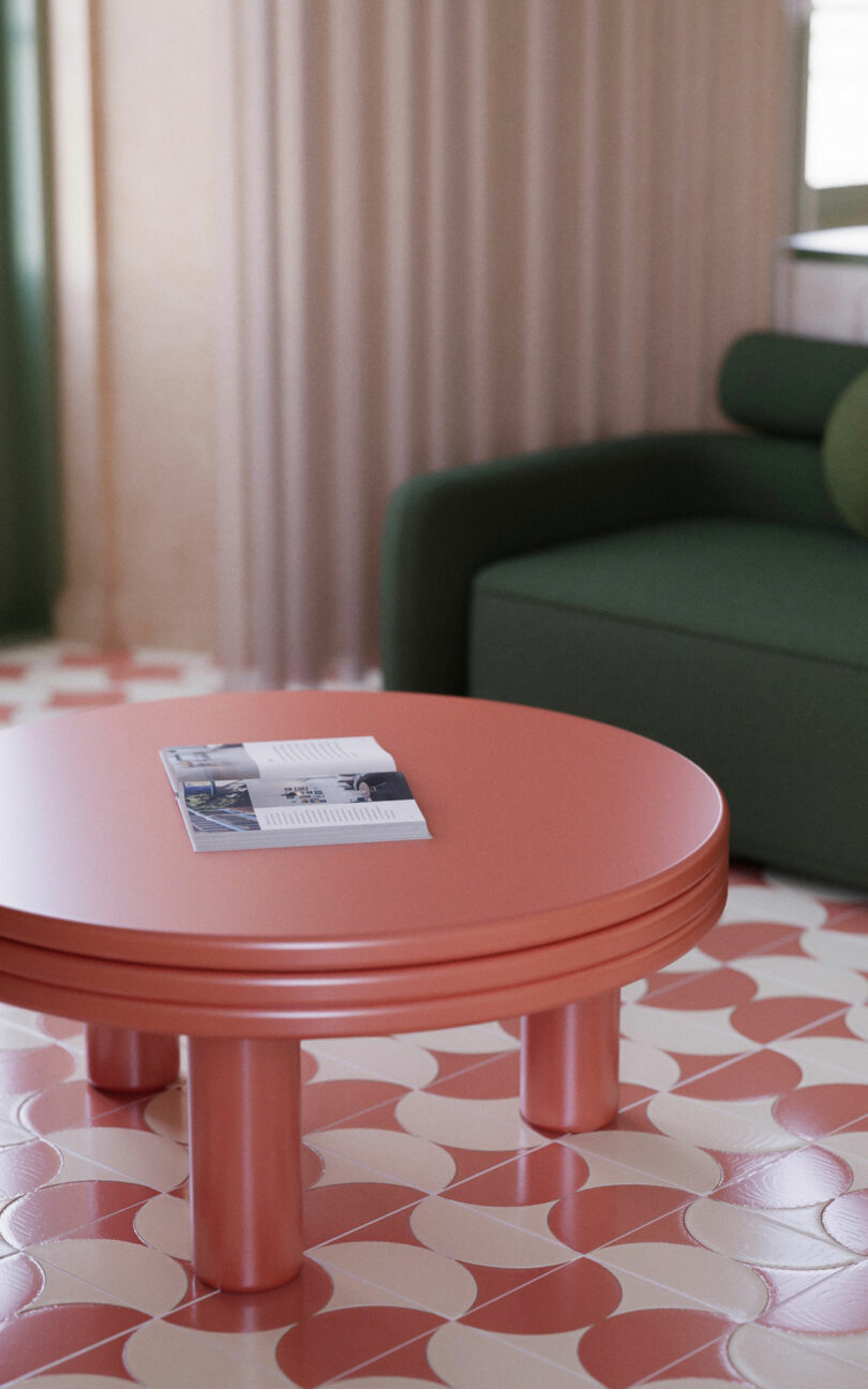 A round pink coffee table with a magazine on top sits on a patterned floor beside a dark green sofa.
