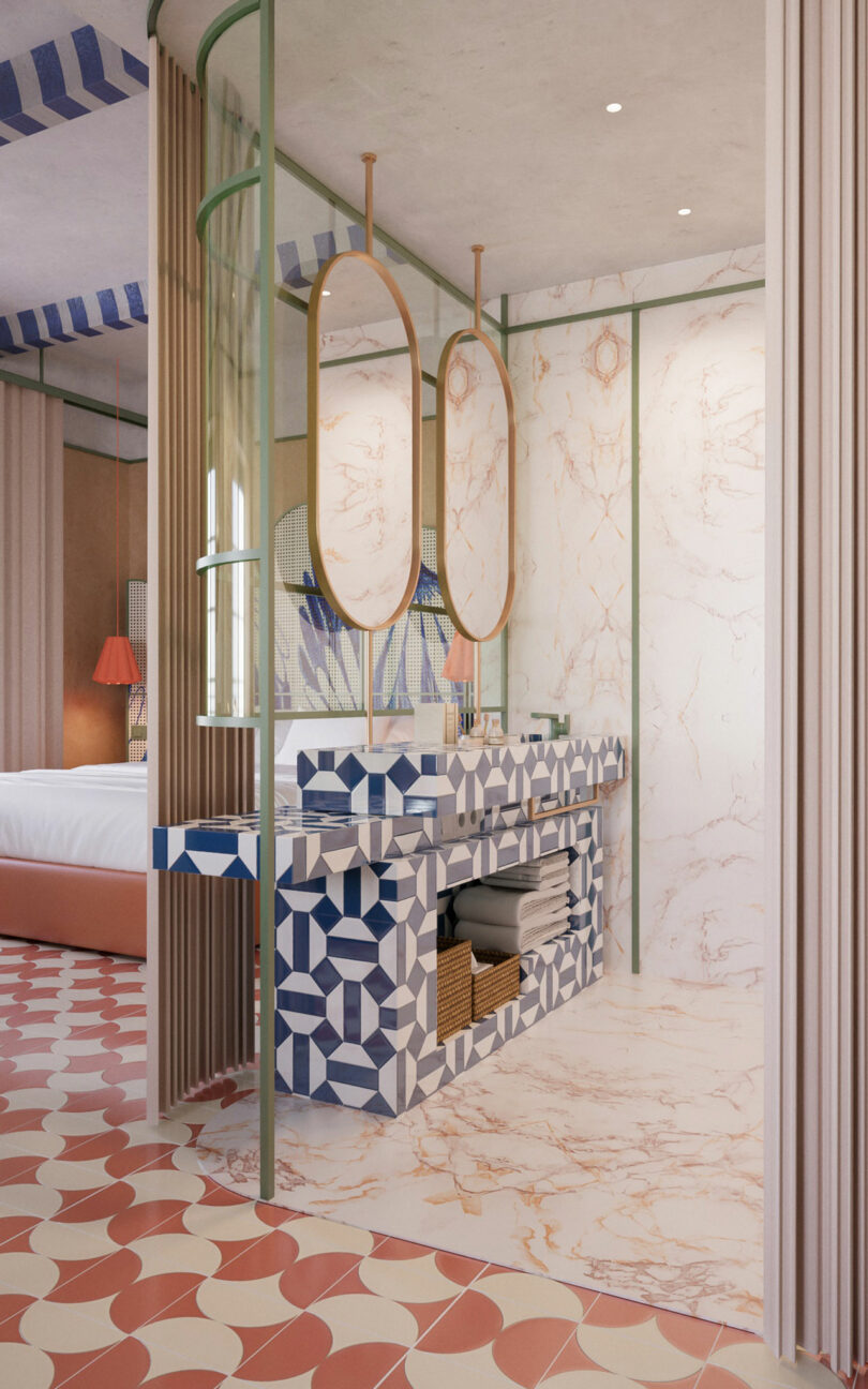 Geometric bathroom with oval mirrors, patterned blue and white vanity, marble walls, and pink tile floor; bedroom visible in background.