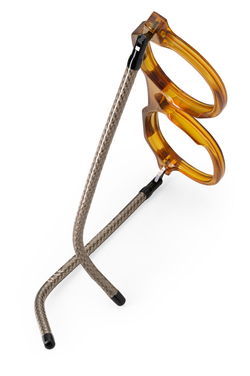 A pair of eyeglasses with round amber-colored frames and flexible, silver braided metal temples, photographed on a white background.