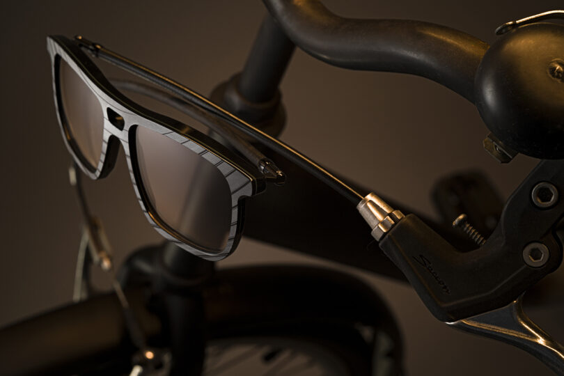 A pair of sunglasses is hanging on the handlebar of a black bicycle, with the bike bell and brake lever visible in the background.