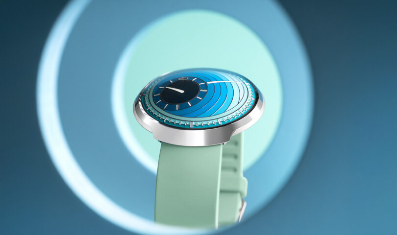 A modern wristwatch with a blue, circular, futuristic dial and a light green strap is displayed against a blue gradient background