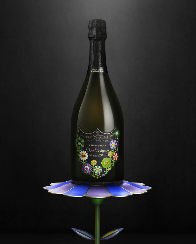 A bottle of Takashi Murakami Dom Perignon Vintage 2013 Champagne with a floral label, displayed on a blue and purple flower-shaped stand against a dark background.
