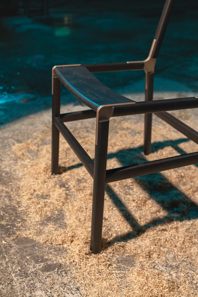 A modern black metal chair with a wooden seat is positioned on a surface covered with sawdust under moody lighting.