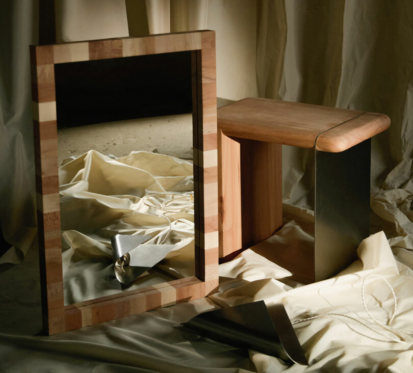 A wooden mirror and a small wooden table are placed on draped cream fabric with a metal trowel, string, and a reflective surface on the floor.