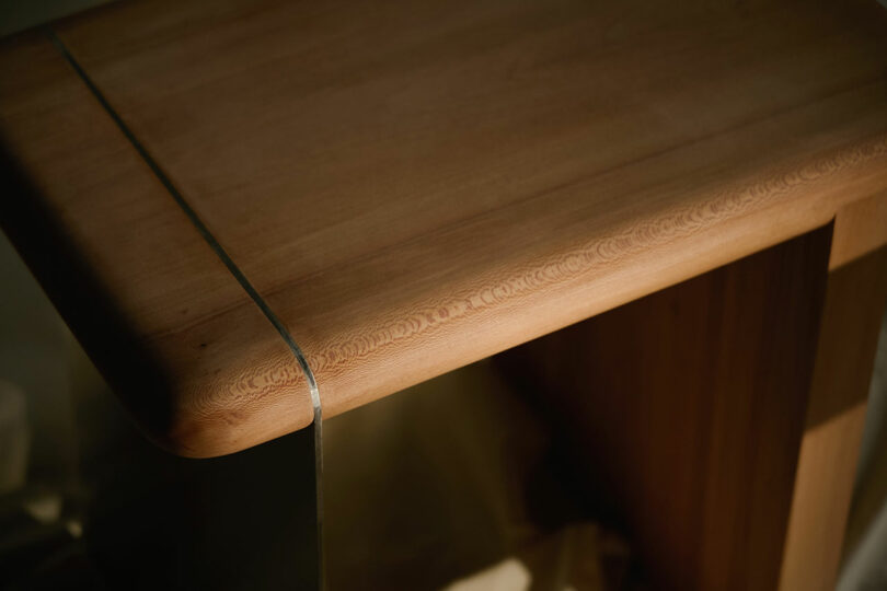 A close-up view of a wooden table corner with a rounded edge and a thin metal strip running along the surface.