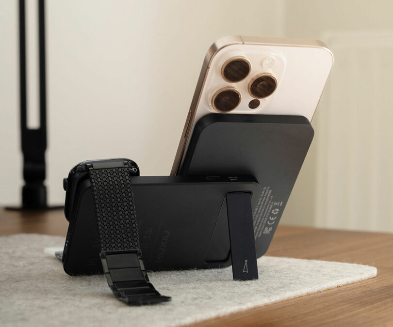 A sleek piece of technology, this smartphone with a metallic strap accessory stands upright on the table using its built-in kickstand, displaying its camera lenses outward.