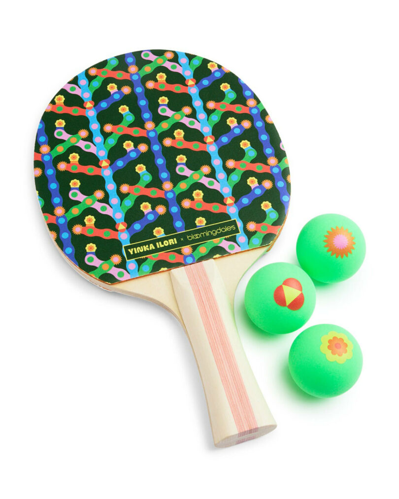 A ping pong paddle with a colorful geometric pattern and a light wooden handle, next to three green ping pong balls with different designs—an eye-catching pick for any Gift Guide 2025.