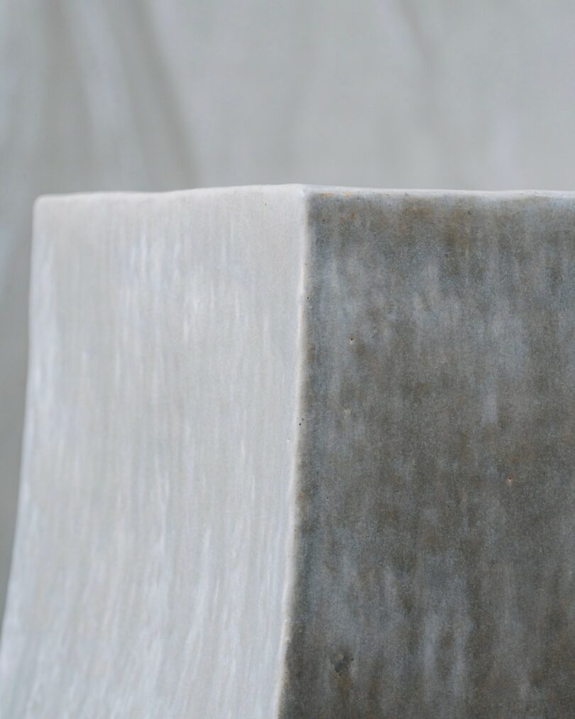 Close-up of the corner of a smooth, rectangular, stone or concrete object with a two-tone surface, set against a blurred neutral background
