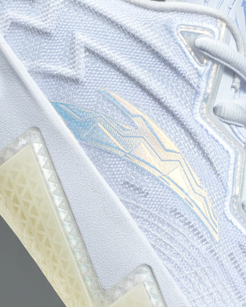 Close-up of a white athletic shoe with iridescent blue and gold geometric patterns and textured sole