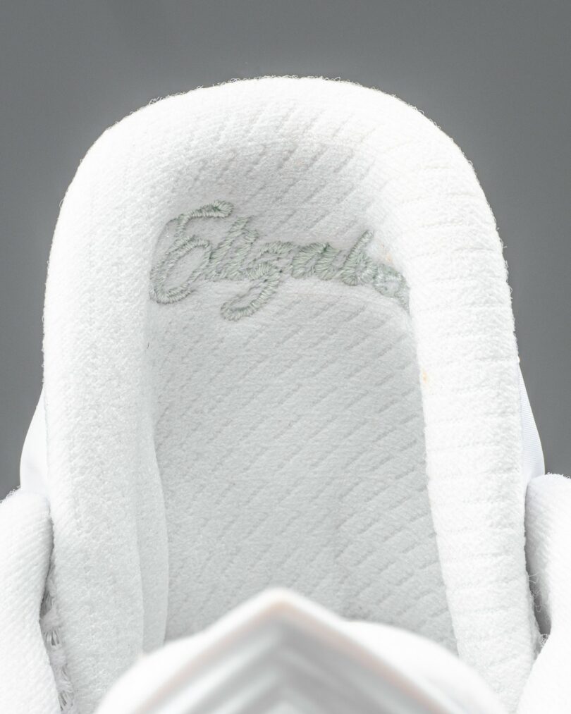 Close-up of a white shoe tongue with the word "Elizabeth" embroidered in light grey stitching on the fabric
