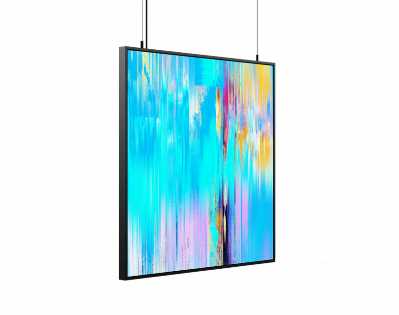 A flat-screen digital display with an abstract, colorful image in blue, yellow, and pink tones, hanging from the ceiling by two cables.