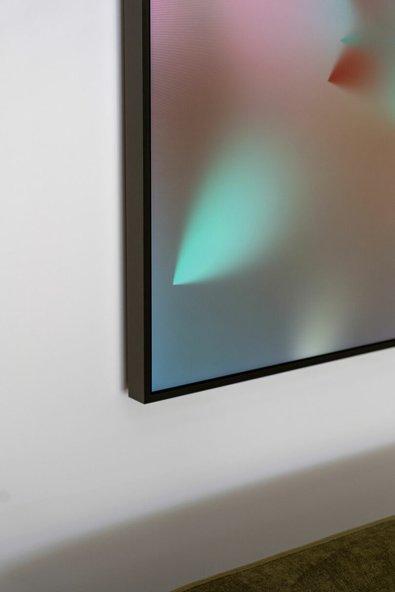 A close-up of a television or monitor mounted on a white wall, displaying a colorful abstract image with green and pink hues.