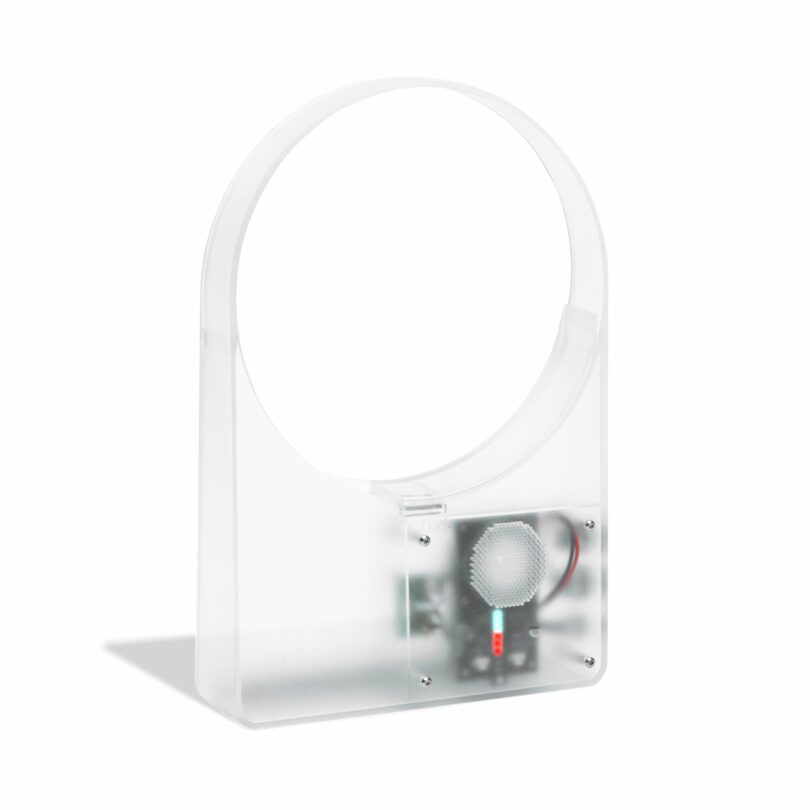 A clear plastic rectangular device with a circular opening on top and an exposed electronic component with a small fan and wires at the bottom.