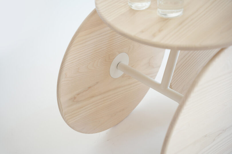 A close-up of a round wooden table with large circular wooden legs and two clear glasses on top, set against a white background.
