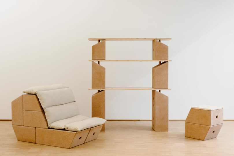 Modular furniture set including a cushioned chair, a small side table, and a three-shelf unit, all made from geometric wooden panels in a minimalist room