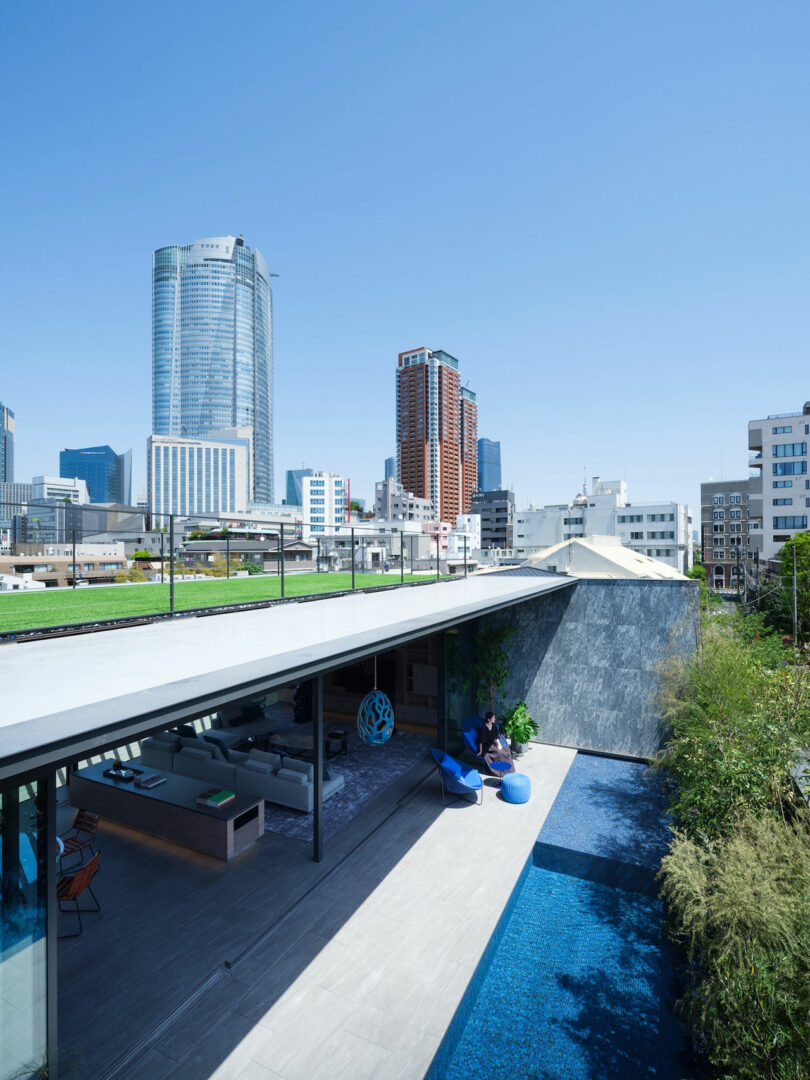 Modern rooftop terrace with seating area and pool, overlooking a cityscape with high-rise buildings under a clear blue sky.