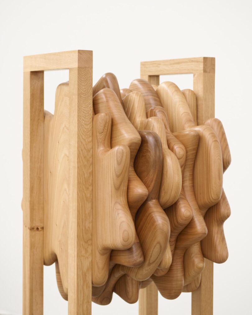 A wooden sculpture featuring a smooth, abstract, cloud-like form encased within a rectangular wooden frame structure