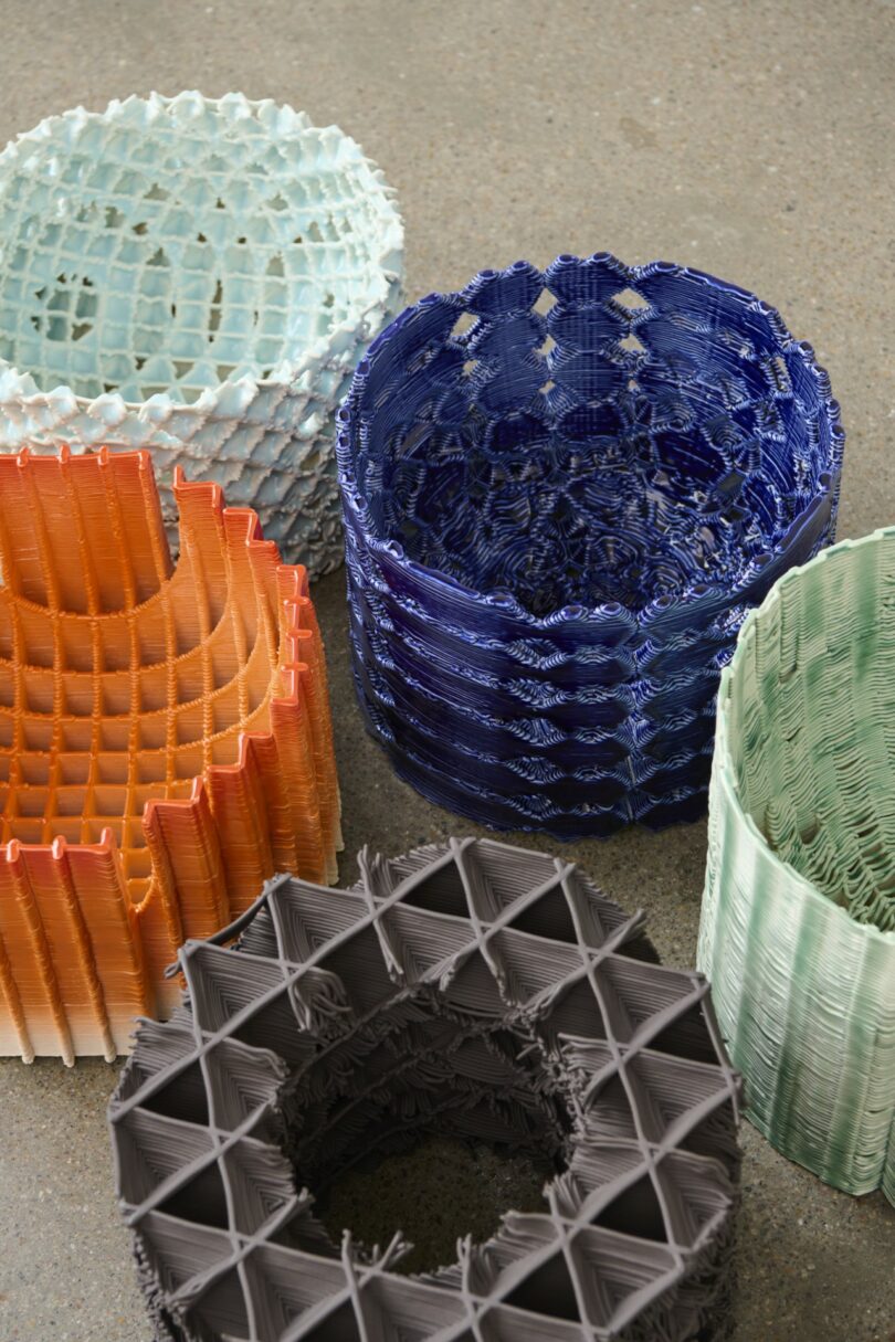 Five colorful, intricately woven baskets of varying shapes and textures are arranged on a smooth, neutral-toned surface