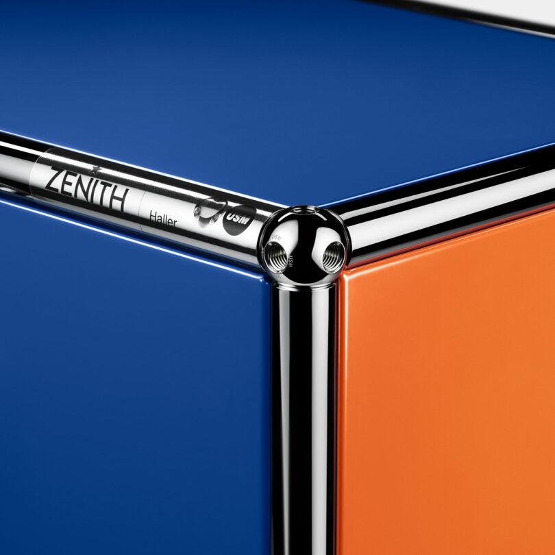 A close-up of a modular furniture corner with chrome metal framing, blue and orange panels, and “ZENITH” branding on the top metal bar.